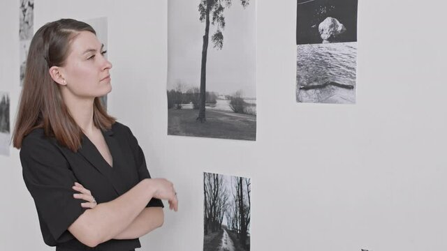 Waist-up of pensive Caucasian female art specialist observing modern collection of black and white photographs, thinking