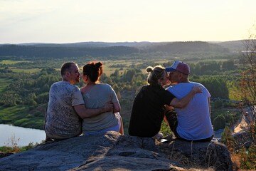 Four friends sitting on edge of mountain at sunset