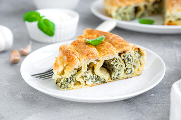 Greek pie spanakopita with feta cheese and spinach on a white plate on a gray concrete background. Copy space.