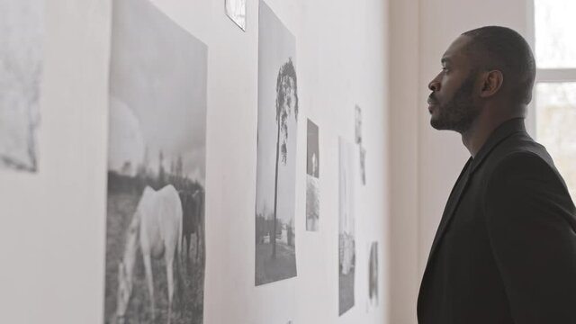 Side view of pensive African male art critic appreciating modern collection of black and white photographs, thinking