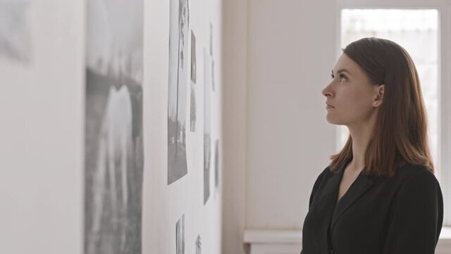 Side view of pensive Caucasian female art critic appreciating modern collection of black and white photographs, thinking