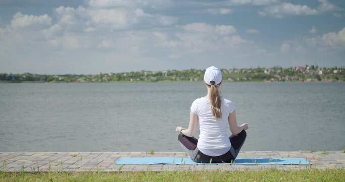 Beautiful young woman practicing yoga near river