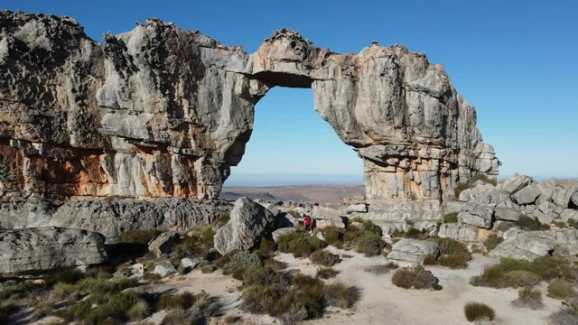 Aerial view of a woman in red jacket walking to Wolfberg Arch near Cederberg hiking trail, Western Cape, South Africa.