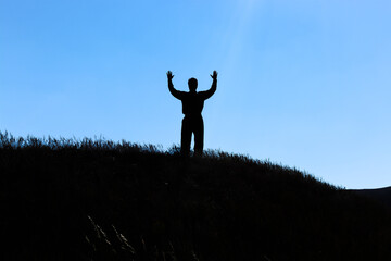 Silhouette of a man. Hands up. Man over the hill. Beam the sun.