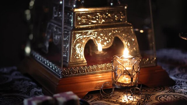 Religion, holidays, concept - Panning along rays of light from window in smoky dusty room falling on altar throne in Christian Orthodox temple with burning candle lamp nearby menorah under chandelier.