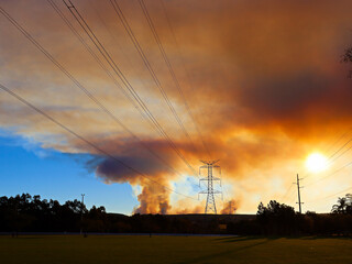 Large overland power lines leading toward the blue mountains with bush fire smoke haze across the setting sun.