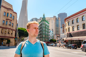 A young man with a backpack in a business center with a view of the Transamerica Tower in San Francisco