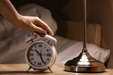 Woman turning off alarm clock in bedroom at night, closeup