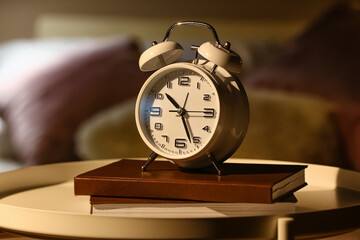 Alarm clock with books on table in bedroom at night, closeup