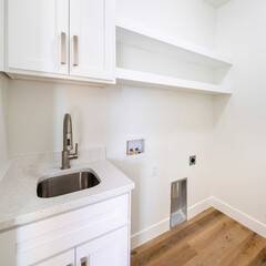 Square frame Empty white laundry room with top storage, laundry connections and dryer vent on the wall