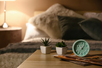 Alarm clock with magazines and houseplants on table in bedroom at night
