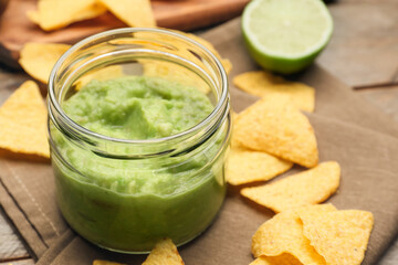 Glass jar with tasty guacamole and nachos on wooden background, closeup