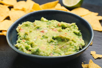 Bowl with tasty guacamole and nachos on dark background, closeup