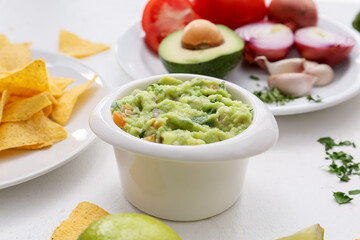 Bowl with tasty guacamole and nachos on light background, closeup