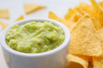 Bowl with tasty guacamole and nachos on light background, closeup