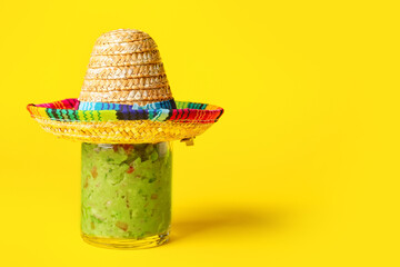 Glass jar with tasty guacamole and sombrero hat on color background