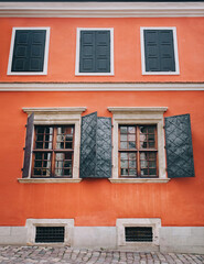 Open metal shutters on the old beautiful windows. Orange facade of the building of the Armenian courtyard in Lviv.