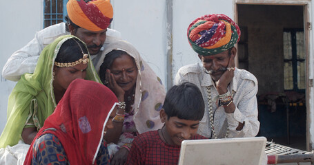 Group of South Asian people in traditional Indian clothing watching a video on a laptop together