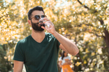 Bearded young adult drinking red wine in the countryside during the grape harvest