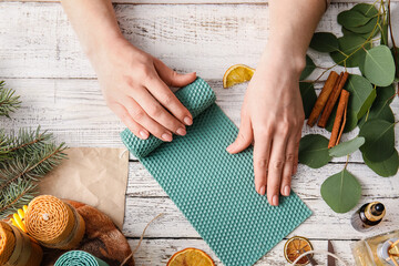 Woman making wax candle on light wooden background