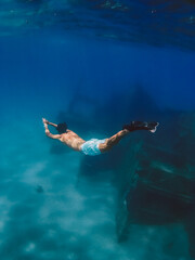 Fototapeta na wymiar Boy snorkels next to a ship wreck submerged in the ocean