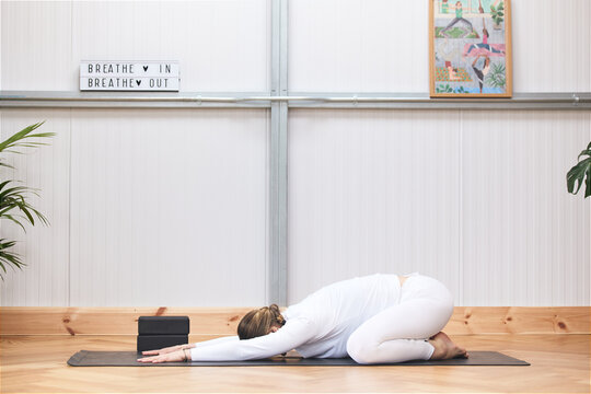 quarpo of woman lying on the floor practicing yoga in a beautiful gymnasium dressed in white