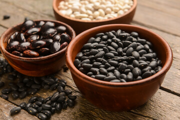 Bowls with different types of beans on wooden background, closeup