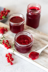 Homemade red currant jam or jelly in glass jars and red currants fresh berries on wooden cutting board.