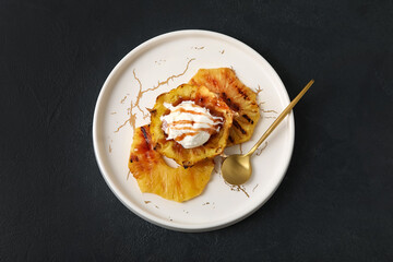 Plate with grilled pineapple slices and ice cream on dark background