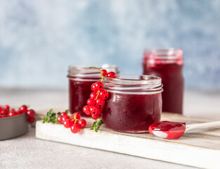 Homemade red currant jam or jelly in glass jars and red currants fresh berries on wooden cutting board.