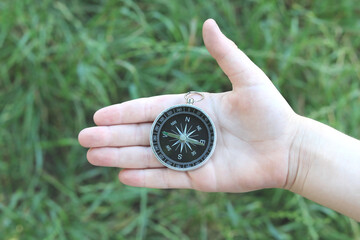 Old classic navigation compass in hand on natural background as symbol of tourism with compass,...
