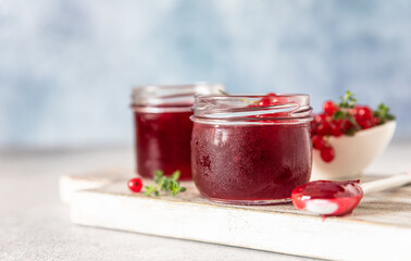 Homemade red currant jam or jelly in glass jars and red currants fresh berries on wooden cutting board.