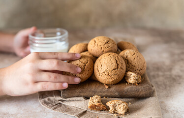 The child's hand takes oatmeal cookies from the board. Brown concrete background. Healthy snack or dessert.
