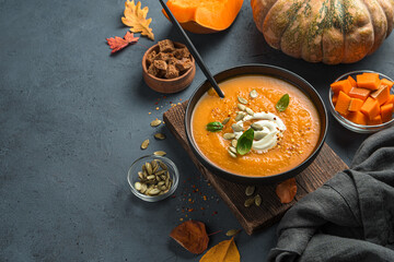 Pumpkin soup with cream and basil on an autumn background.