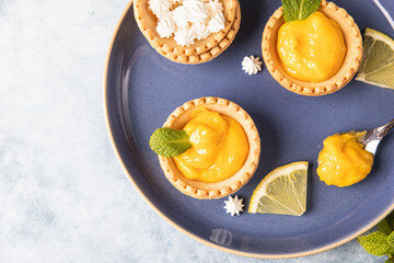 Lemon curd mini tarts decorated with mint and lemon slices on blue ceramic plate. Top view.