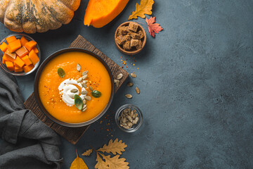 Pumpkin cream soup in a black bowl on an autumn background.