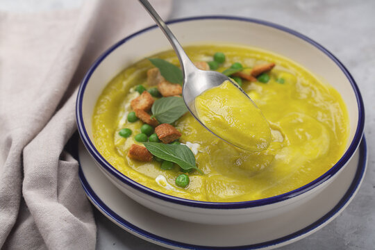 Vegetable puree soup with a tablespoon with crackers and basil