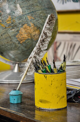 Many school ink pens and an inkwell on the desk with a globe behind it in a 50s classroom