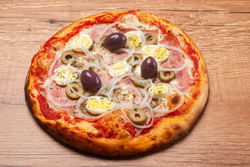 Portuguese pizza, with ham, cheese, eggs, onion and black olives, served on a rustic wooden table.