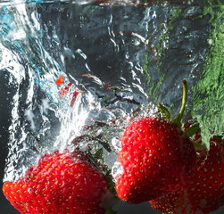 ripe strawberries fall into the water lifting splashes and air bubbles