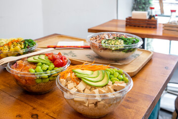 Poke bowl with diced tofu, edamame beans, avocado slices, base white rice and a container to serve at home while waiting on a restaurant table