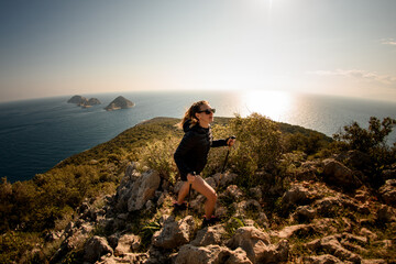 panoramic view of woman with hiking poles walking along the trail at seascape background