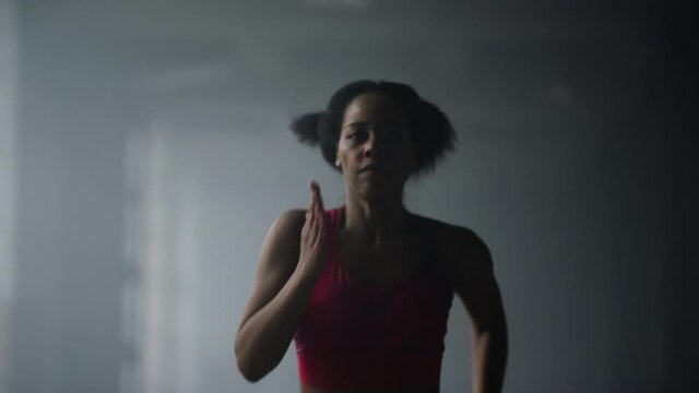 Sporty girl jogging in gym. Woman running fast in dark corridor of loft building