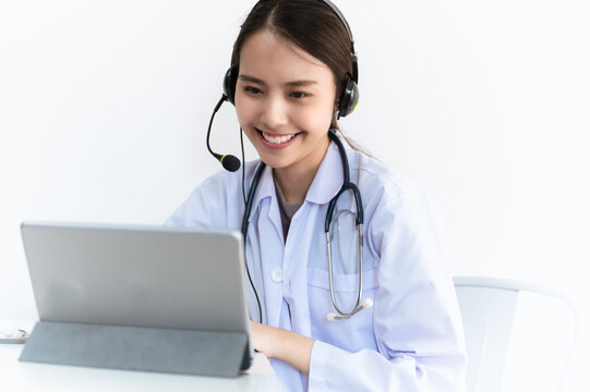 Portrait photo of young beautiful Asian doctor video remote conference call online with patient for social distancing due to covid-19 pandemic. Technology, health care new normal online telehealth.