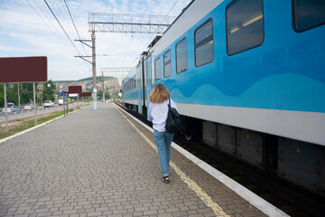 Beautiful young girl walks next to a blue train at the railway station perspective