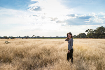 Naklejka na ściany i meble Young adult smiling Mexican woman standing in a dry grassy meadow looking at the camera