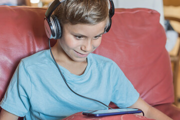 the boy is smiling and listening to music,playing,doing homework online with smartphone.Pupil in headphones.