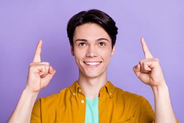 Photo of cool brunet young guy point look up wear yellow shirt isolated on violet color background