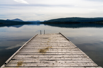 calm lake with reflections of mountains and sky and a wooden dock in the foreground