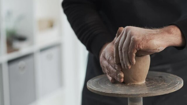 Potter forming cup from clay on potter's wheel at light workhouse